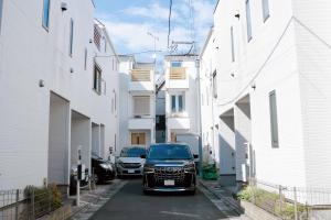 two cars parked in a alley between white buildings at SunRise STAY Haruna in Tokyo