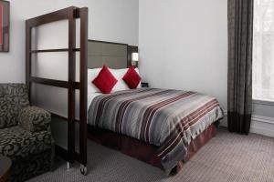 Un dormitorio con una cama con almohadas rojas y una silla en The Grand at Trafalgar Square, en Londres