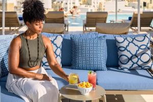 a woman sitting on a couch with a bowl of fruit at Novotel Malta Sliema in Il-Gżira
