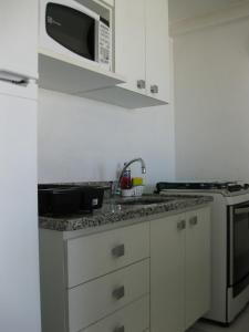 a white kitchen with a sink and a microwave at Porto Real Suites in Mangaratiba