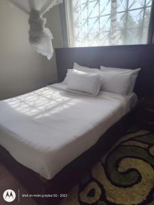 Una cama con sábanas y almohadas blancas y una ventana. en Sonkoyaz bed and breakfast, en Entebbe