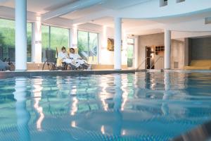 two women sitting in chairs next to a swimming pool at Hotel Leonhard in Leogang