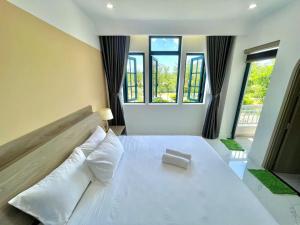 a bedroom with a large white bed with pillows and windows at KNK villa in Bình Tú