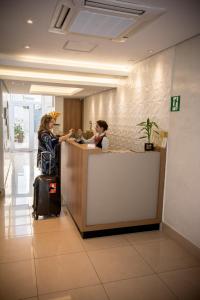 Eine Frau mit einem Koffer, der an einer Theke in einem Büro steht. in der Unterkunft Hotel Estação Paraíso - ao lado do Metrô Paraíso e 600m da Av Paulista in São Paulo