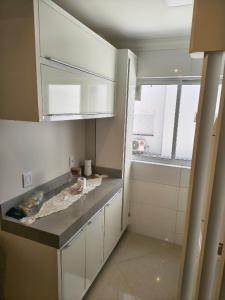 eine kleine Küche mit weißen Schränken und einem Fenster in der Unterkunft Apartamento aconchegante com ar, secadora e adega in Piratuba