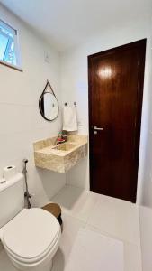 a bathroom with a toilet and a wooden door at Casa Oxente - 2da praia condominio com piscina in Cayru