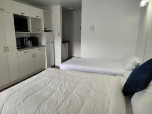 a white bedroom with two beds and a kitchen at Hébergements ASLC Baie-Comeau in Baie-Comeau