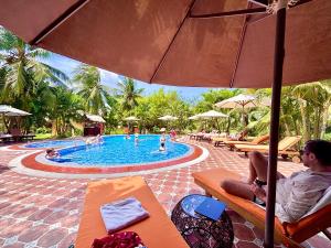 a man sitting on a bench next to a swimming pool at Mango Home Riverside Eco - Resort in Ben Tre