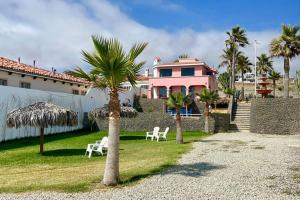 a pink house with two palm trees and white chairs at Oceanfront - Casita Rosa in Puerto Nuevo