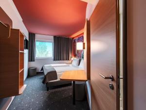 a hotel room with a bed and a desk and a door at B&B HOTEL München-Messe in Aschheim