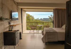 ein Schlafzimmer mit einem Bett und ein Balkon mit einem Tisch in der Unterkunft Calliandra Suítes Minimalistas in Alto Paraíso de Goiás