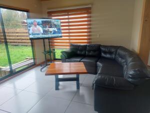 a living room with a black leather couch and a tv at Beautiful Cabin in Pucon 4D3B in El Cerrillo