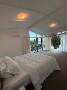 - une chambre blanche avec un grand lit et des fenêtres dans l'établissement Private Beachfront Haven with Starlink & Panoramic Views, à Kerikeri