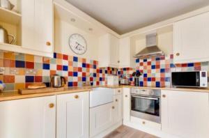a kitchen with white cabinets and a clock on the wall at Pilots House Aldeburgh in Aldeburgh