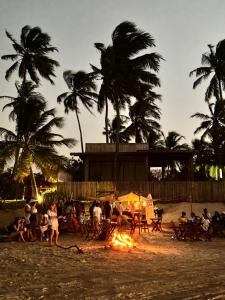 a group of people sitting around a fire on the beach at Maré Mansa Suítes Icaraizinho in Amontada