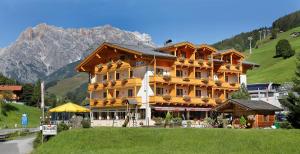 a large building on a hill with mountains in the background at Hotel Bachschmied in Maria Alm am Steinernen Meer