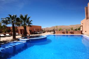 a large blue swimming pool with palm trees and mountains at Hotel Xaluca Dades in Boumalne