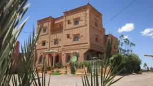 un grand bâtiment en briques avec des arbres devant lui dans l'établissement Riad Dar Barbara, à Ouarzazate