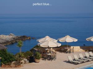 a group of tables and chairs with umbrellas and the ocean at Giorgi's Blue Apartments in Kalathas