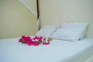 a bed with white pillows and purple flowers on it at Low budget double room in Paje in Paje