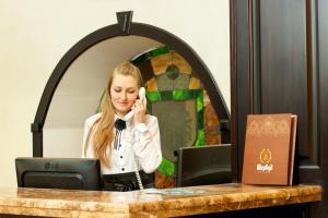 a woman talking on a phone at a desk with a computer at Sherwood Hotel in Dovgomostys”ka