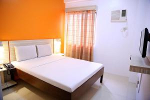 a bedroom with a white bed with an orange wall at Travelbee Business Inn in Cebu City
