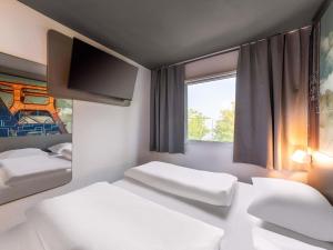 a room with two beds and a window and a tv at B&B HOTEL Würzburg-Ost in Würzburg