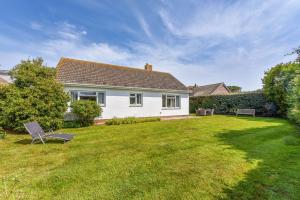a white house with a yard with a bench at 21 Owers Way, West Wittering in West Wittering