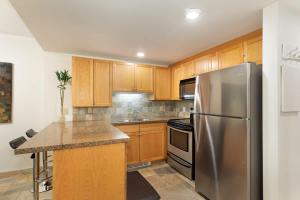a kitchen with wooden cabinets and a stainless steel refrigerator at Woodrun Lodge 216 | Renovated Ski-In Ski-Out Condo w/ Free Parking, Pool, Hot Tub, & Gym in Whistler