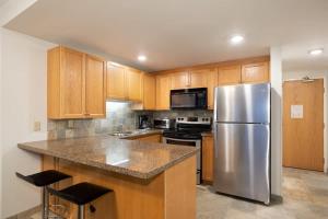 a kitchen with wooden cabinets and a stainless steel refrigerator at Woodrun Lodge 216 | Renovated Ski-In Ski-Out Condo w/ Free Parking, Pool, Hot Tub, & Gym in Whistler +21 photos