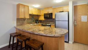 a kitchen with a counter with stools and a refrigerator at Woodrun Lodge 217 | Ski-In Ski-Out Condo - Walk to Upper Village w/ Hot Tub, Pool + Free Parking in Whistler