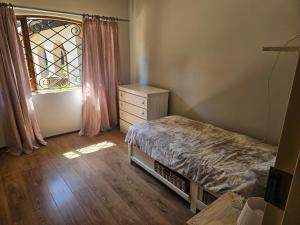 ein Schlafzimmer mit einem Bett, einer Kommode und einem Fenster in der Unterkunft Family Home in Roodepoort + 7 Fotos