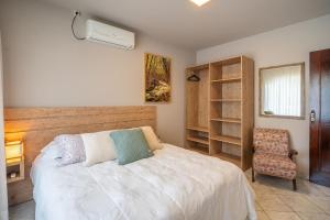 ein Schlafzimmer mit einem weißen Bett und einem Stuhl in der Unterkunft Casa térrea com 03 quartos em Canto Grande in Canto Grande