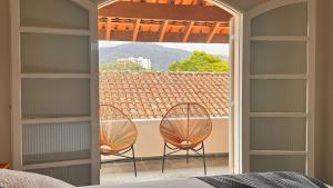 a bedroom with two chairs and a balcony with a view at Suítes Aqui é Seu Lugar Itaguá in Ubatuba