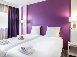 two beds in a hotel room with purple walls at Mercure Strasbourg Aéroport in Ostwald