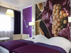 a hotel room with a bed and a painting of grapes at Mercure Strasbourg Aéroport in Ostwald