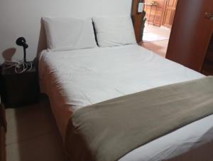 un lit avec des draps blancs et des oreillers dans une chambre dans l'établissement Casa de Madeira no Centro, à Miguel Pereira