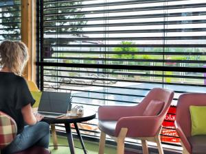 a woman sitting at a table with a laptop in front of a window at Ibis Styles Colmar Nord in Colmar