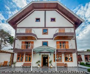 an exterior view of a white building with a balcony at Pousada Vilage Inn Campos do Jordão in Campos do Jordão