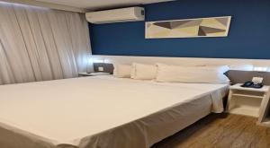 a bedroom with a large white bed with a blue wall at Transamerica Fit Contagem in Contagem