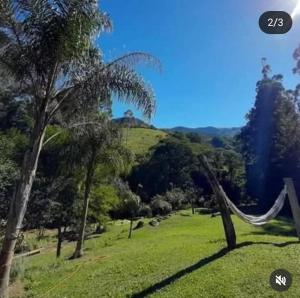 a hammock in a field with trees and a hill at Pousada Sitio do Bau in São Bento do Sapucaí