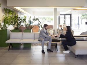 a man and woman sitting on a couch in a lobby at Novotel Lausanne Bussigny in Lausanne