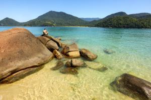 a man sitting on some rocks in the water at Pousada Ilhas de Ubatuba in Ubatuba