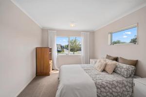 a white bedroom with a bed and a window at Holden's Bay Honey - Relax by the lake in Rotorua
