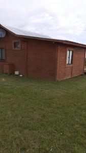 a brown building with a grass field next to it at Casa para 5 personas in Juan L. Lacaze