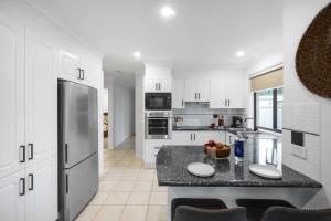 a kitchen with white cabinets and a stainless steel refrigerator at Beach Holiday Villa Jervis Bay in Vincentia