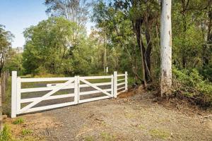 a white fence on a dirt road with trees at Van Demears Escapes by Tiny Away in Tamborine