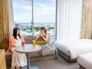 two women sitting in a hotel room with a window at Nishitetsu Resort Inn Naha in Naha
