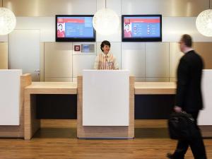 a woman standing at a counter in an airport at ibis Aachen Marschiertor - Aix-la-Chapelle in Aachen