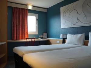 a hotel room with two beds and a desk at Ibis Paris Nord Villepinte Parc des Expositions in Roissy-en-France